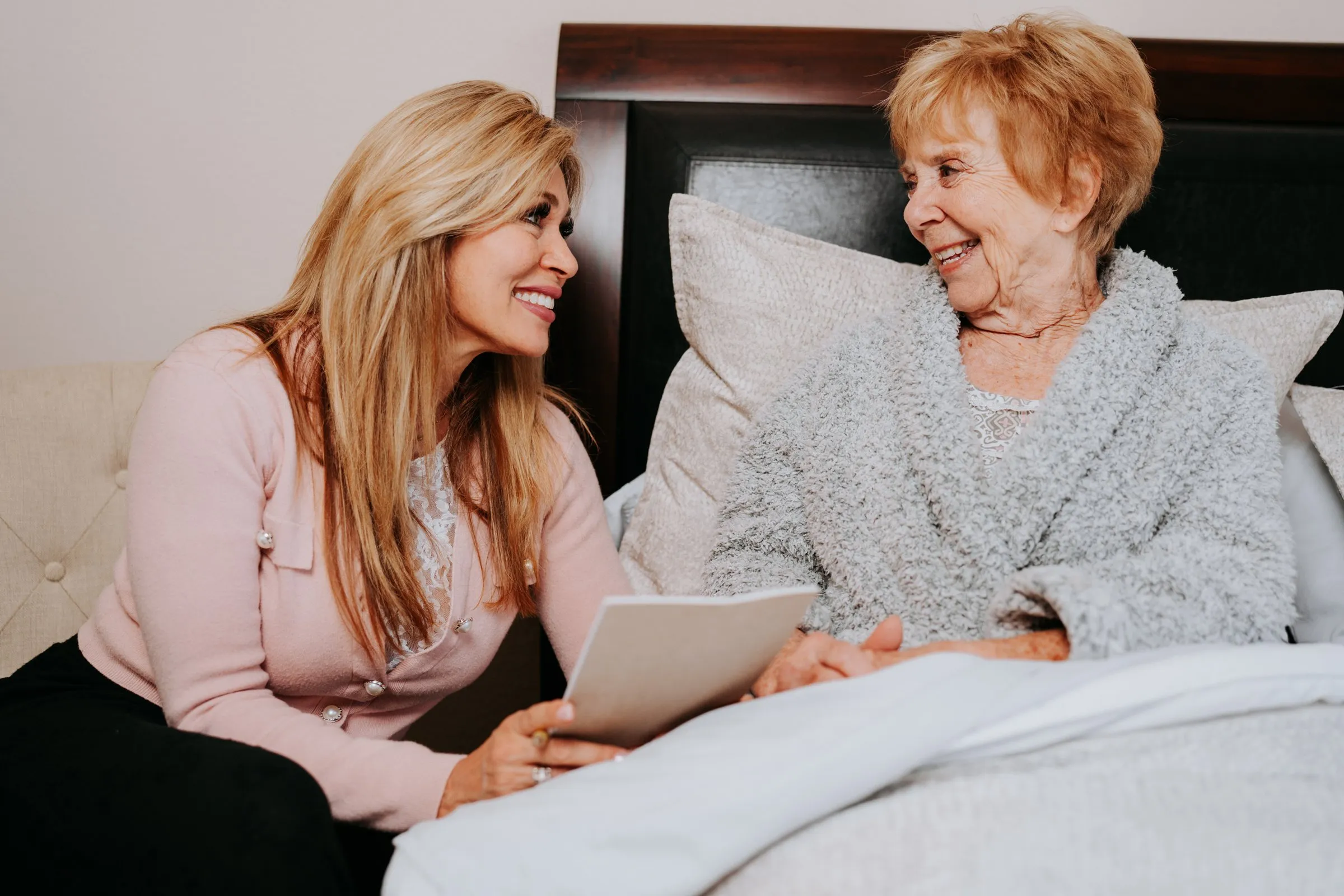 Michelle listening and taking notes beside an elderly client resting in bed