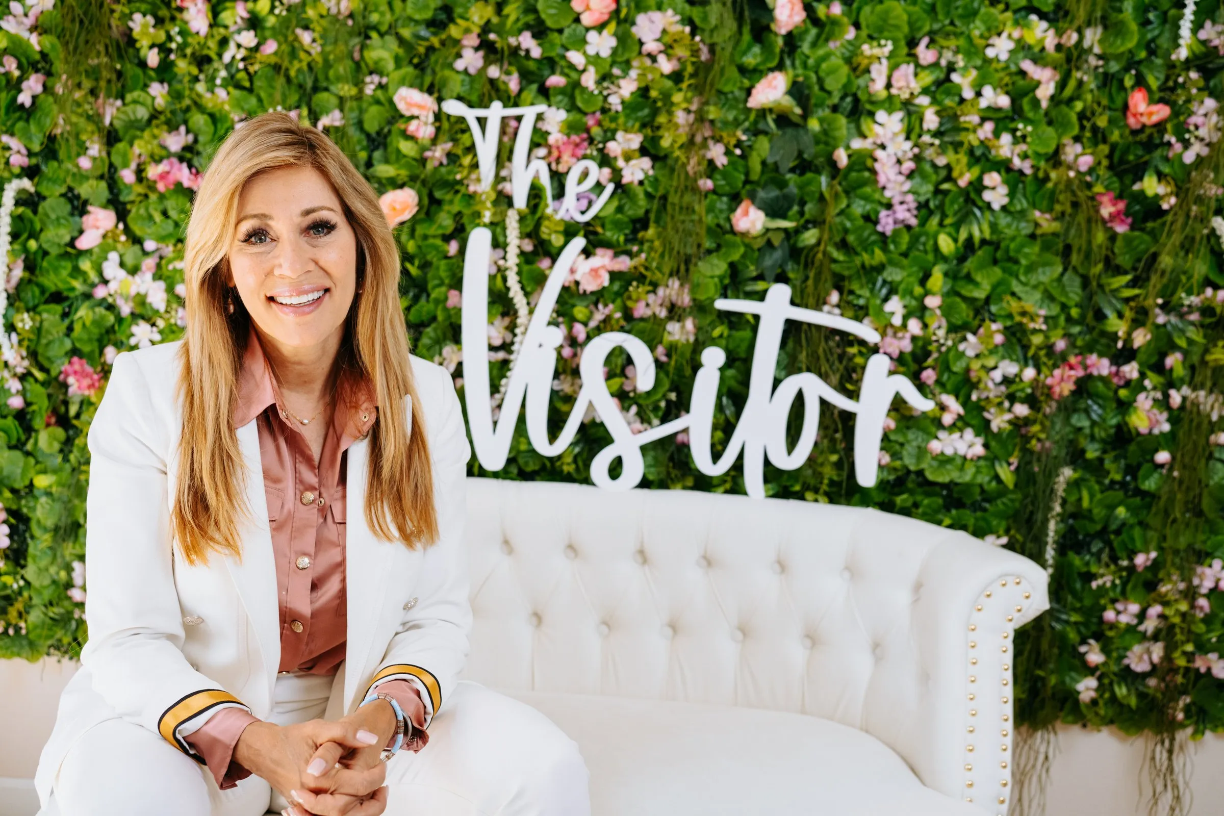 Michelle in a white suit in front of The Visitor flower wall