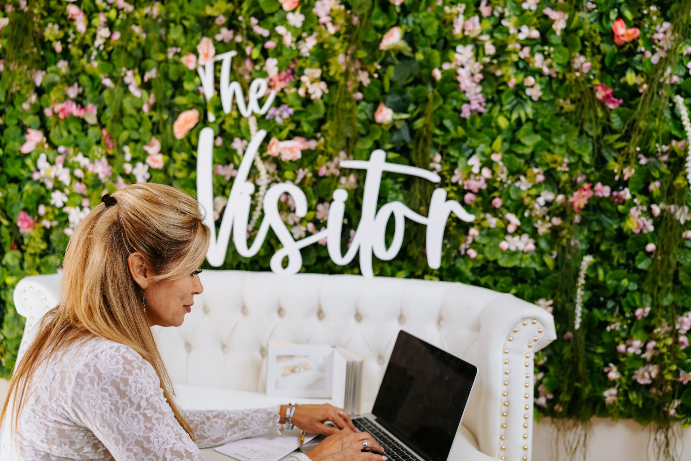 Michelle working on a laptop in front of The Visitor flower wall